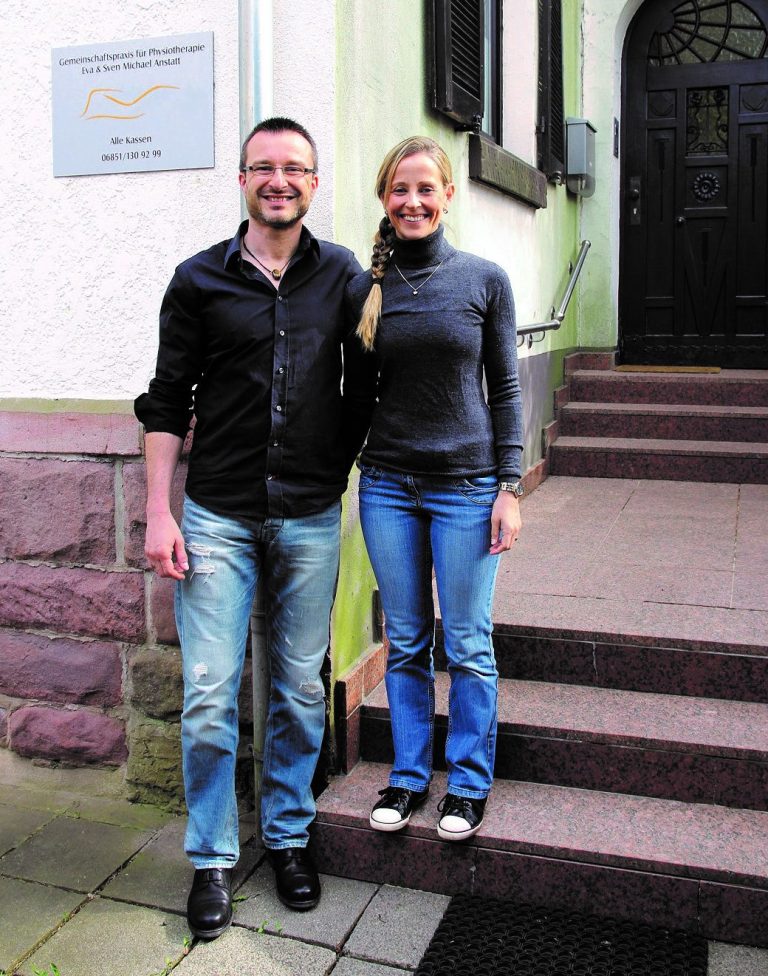 Sven Michael und Eva Anstatt auf einer kleinen Treppe vor dem Praxiseingang und dem Praxis-Schild.