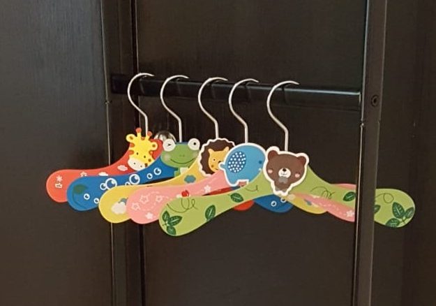 Fünf bunte Kinder-Kleiderbügel mit Motiven von Tierköpfen; sie hängen an einer schwarzen Kleiderstange.