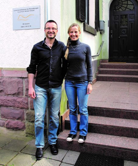 Sven Michael und Eva Anstatt auf einer kleinen Treppe vor dem Praxiseingang; daneben an der Hauswand ist das Praxis-Schild.